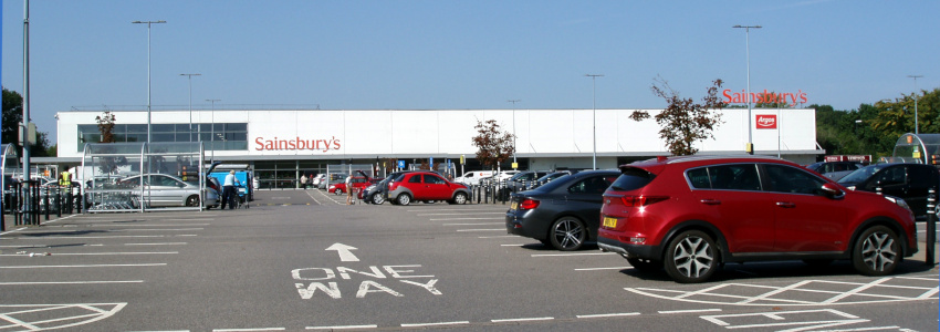A wide, short white building with the word Sainsbury's in large orange letters, a car park in front.